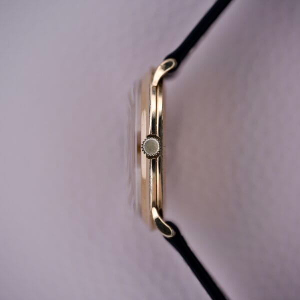 A close-up side view of the Bulova Gold Sunburst Dial & Case Cal. 11AFC, a thin wristwatch with a black strap and Gold Sunburst Dial, shown against a light background.