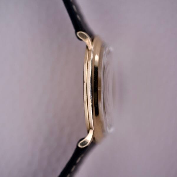 Side view of the Bulova Gold Sunburst Dial & Case Cal. 11AFC wristwatch with black leather strap, domed glass, and gold sunburst dial against a light background.
