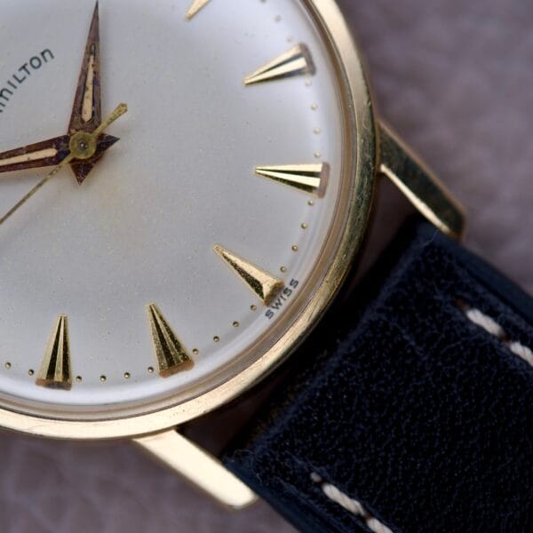 Close-up of a vintage Hamilton Sea-Scape Sunburst Dial Manual Wind Cal. 671 wristwatch with a gold case and black leather strap.