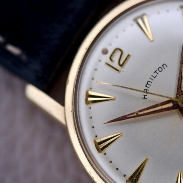 Close-up of a Hamilton Sea-Scape Sunburst Dial Manual Wind Cal. 671 wristwatch, gold case with numbers 12, 2, and 4 visible, paired with a black leather strap.