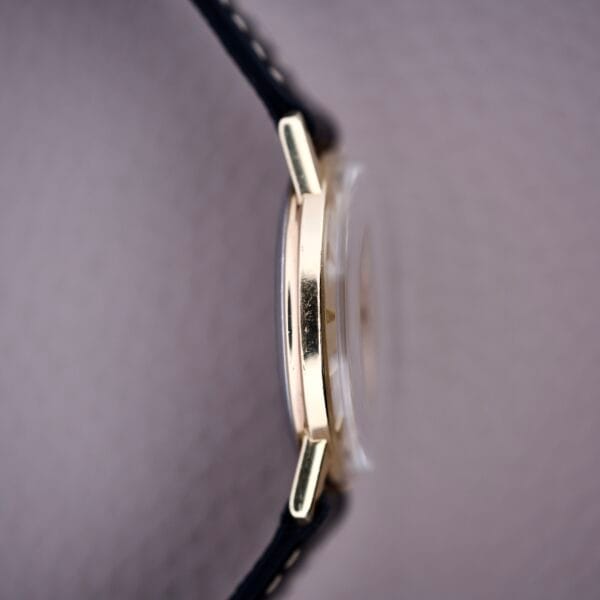 Close-up side view of a Hamilton Sea-Scape Sunburst Dial Manual Wind Cal. 671 gold case with black leather strap, set against a light background.