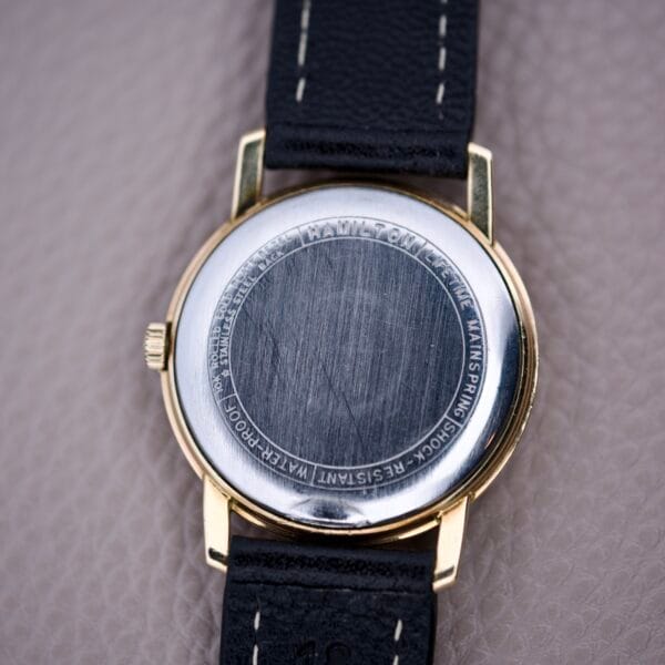 The Hamilton Sea-Scape Sunburst Dial Manual Wind Cal. 671 wristwatch is shown with a black leather strap on a textured beige surface, featuring its reliable Cal. 671 movement and distinctive sunburst dial.