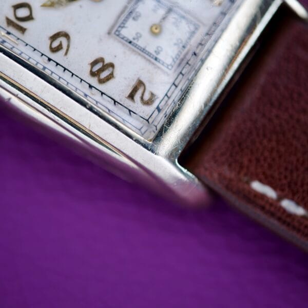 Close-up of a 1936 Lord Elgin Star Dial Tank Style wristwatch, Grade 531, with a brown leather strap, set against a purple background.