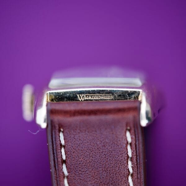 Close-up of a 1936 Lord Elgin Star Dial Tank Style Case Manual Wind Grade 531 with a brown leather strap and 14K gold filled engraving, displayed against a purple background.