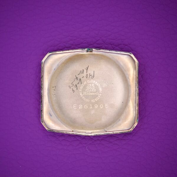 Square gold 1936 Lord Elgin Star Dial Tank Style Case Manual Wind Grade 531 watch case back with engraved text, displayed on a textured purple surface.