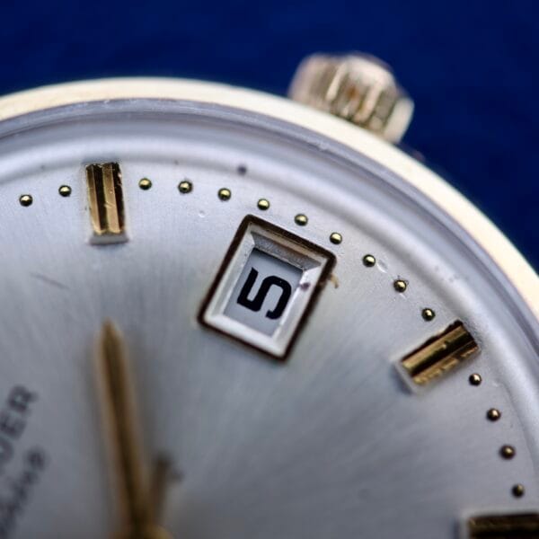Close-up of a Wittnauer Geneve Manual Wind Date & Sunburst Dial watch, featuring a silver face, gold hour markers, blue sunburst dial, and date display set to 5.