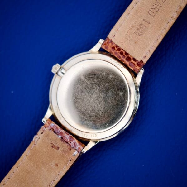 A close-up of the Wittnauer Geneve Manual Wind Date & Sunburst Dial wristwatch with a leather strap on a blue background, highlighting its refined design.