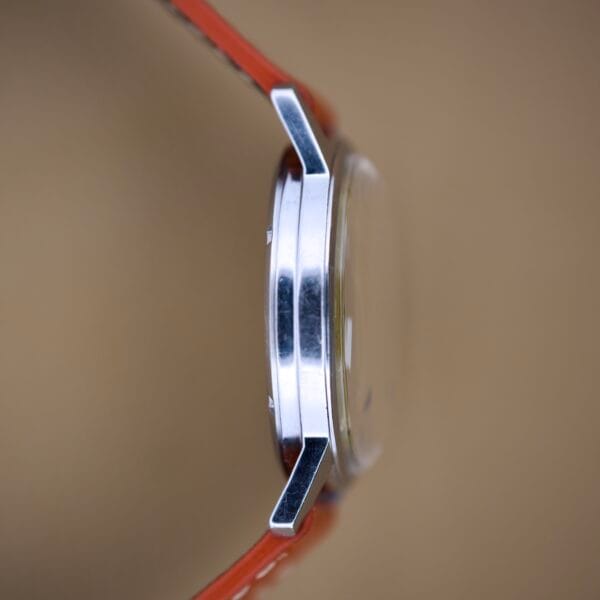 Side view of the Helbros Invincible 21 Jewels Manual Wind Stainless Steel Case wristwatch with orange strap on a neutral brown background.