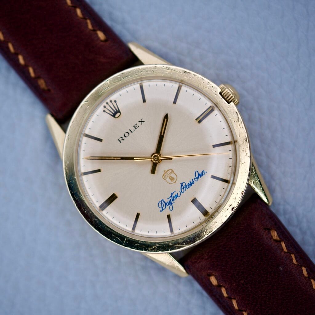 The Rolex Presentation Watch Ref. 7002 features a Cal. 1520 movement, a 14k gold filled case, brown leather strap, and “Dayton Brass Inc.” printed on the dial.