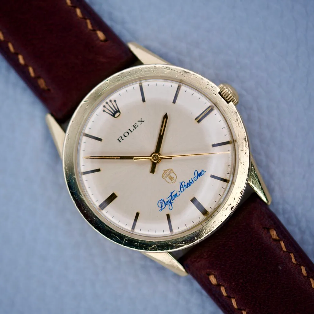 The Rolex Presentation Watch Ref. 7002 features a Cal. 1520 movement, a 14k gold filled case, brown leather strap, and “Dayton Brass Inc.” printed on the dial.