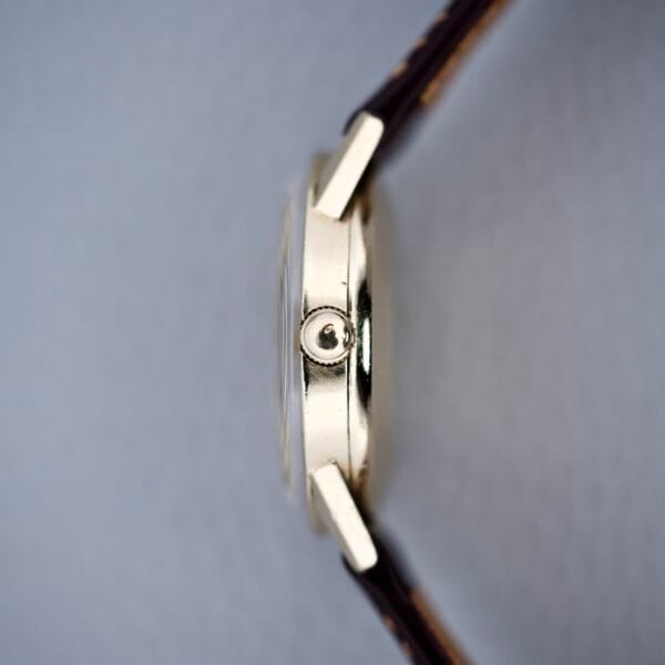 Side view of a Rolex Presentation Watch Ref. 7002 in 14k gold filled case with a brown leather strap, focusing on the crown and elegant Cal. 1520 movement, set against a grey background.