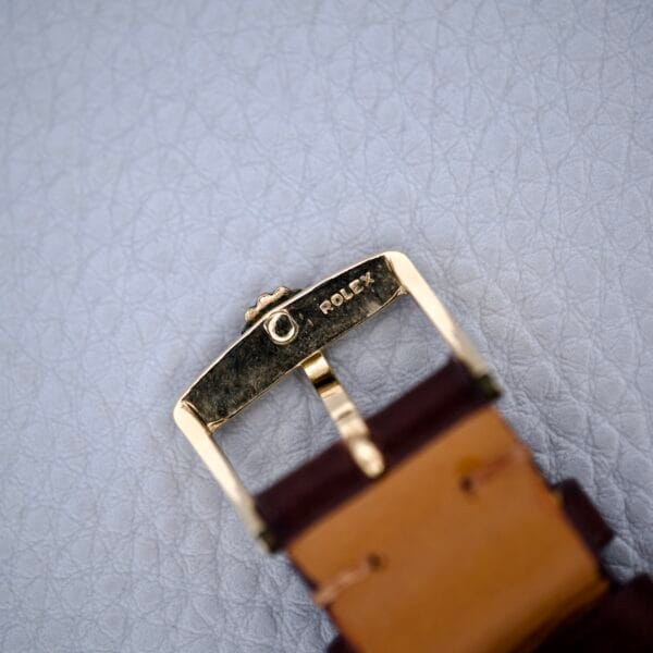 Close-up of the vintage Rolex Presentation Watch Ref. 7002 with a 14k Gold Filled buckle and brown leather strap, Cal. 1520, displayed on a textured grey surface—an elegant classic detail.