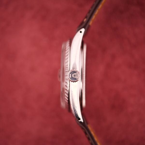 Side view of a Rolex Datejust 1603 Silver Dial Alpha hands wristwatch with a leather strap, set against a textured pink background.