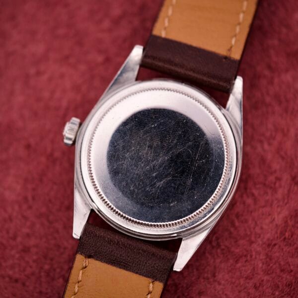 A Rolex Datejust 1603 Silver Dial Alpha hands watch with a brown leather strap is shown from the scratched back, resting on a red textured surface.