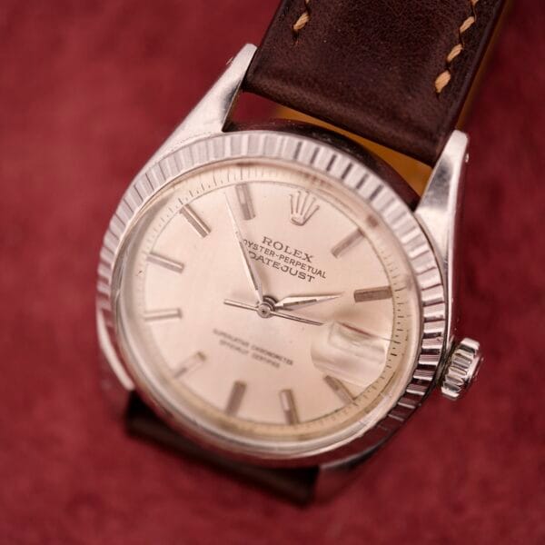 A Rolex Datejust 1603 Silver Dial Alpha hands watch with a brown leather strap rests elegantly on a textured red surface.