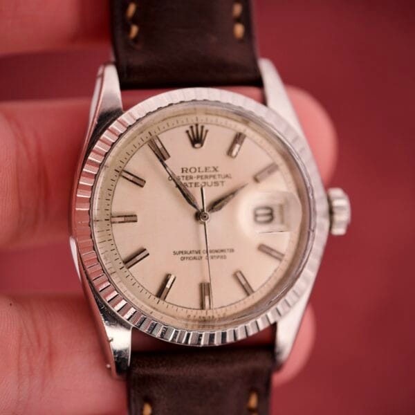 A hand holding a Rolex Datejust 1603 Silver Dial Alpha hands watch with a brown leather strap and silver bezel.