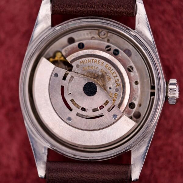 Close-up of a Rolex Datejust 1603 Silver Dial with Alpha hands, showcasing its intricate movement and engraved text, set against a red background.