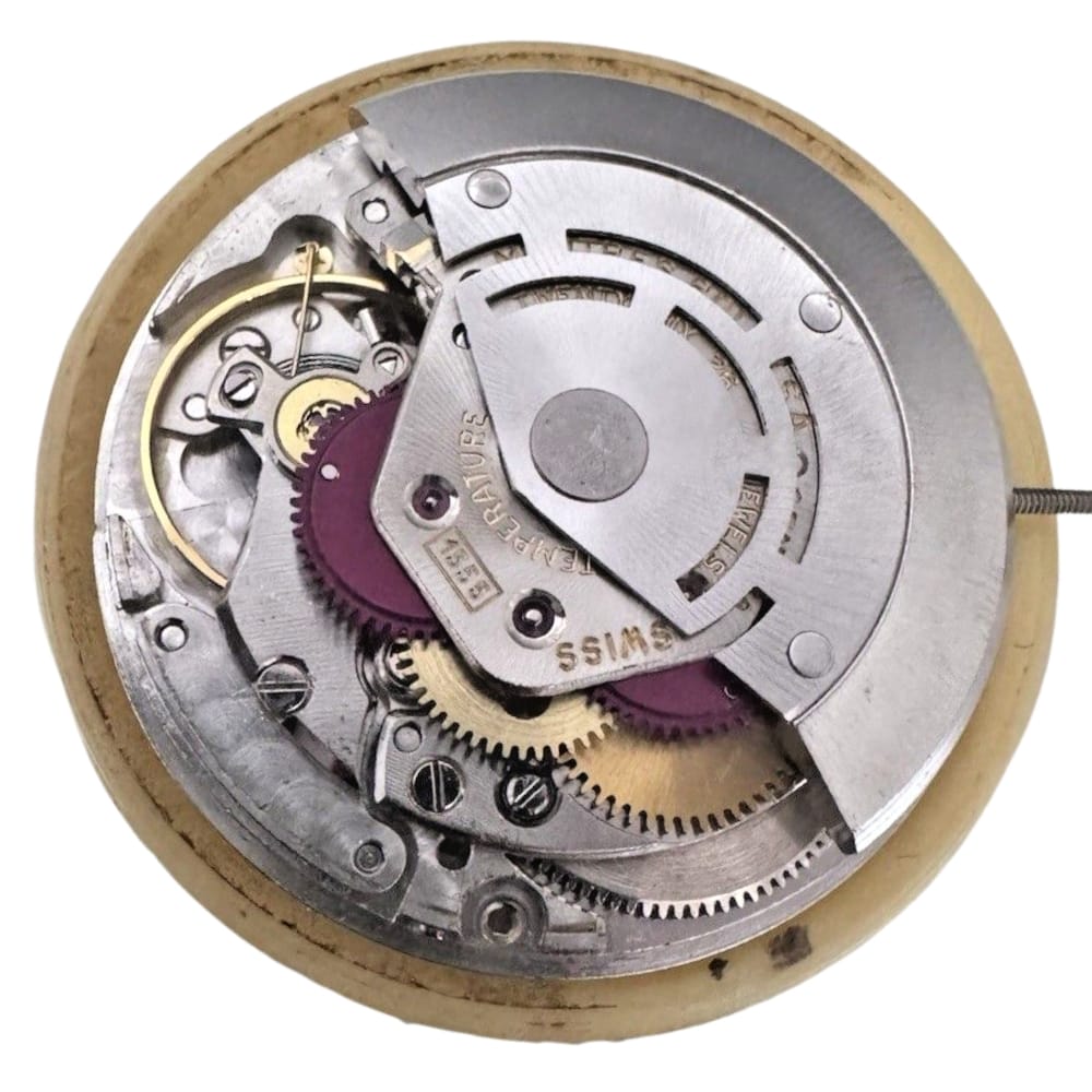 Close-up of a watch movement with visible gears, metal components, and engraved markings.