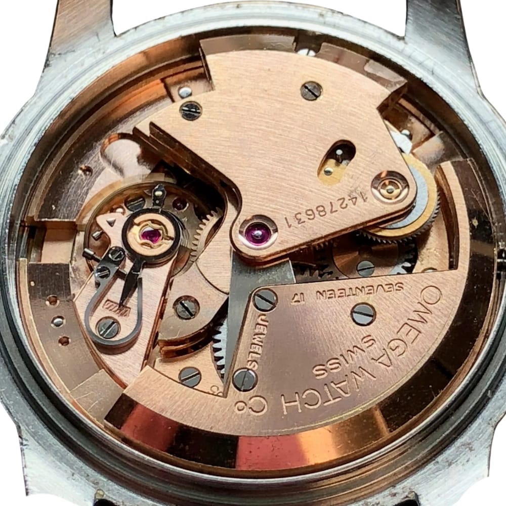 Close-up of an Omega watch movement showing gears, screws, and engraved text on the metal components.