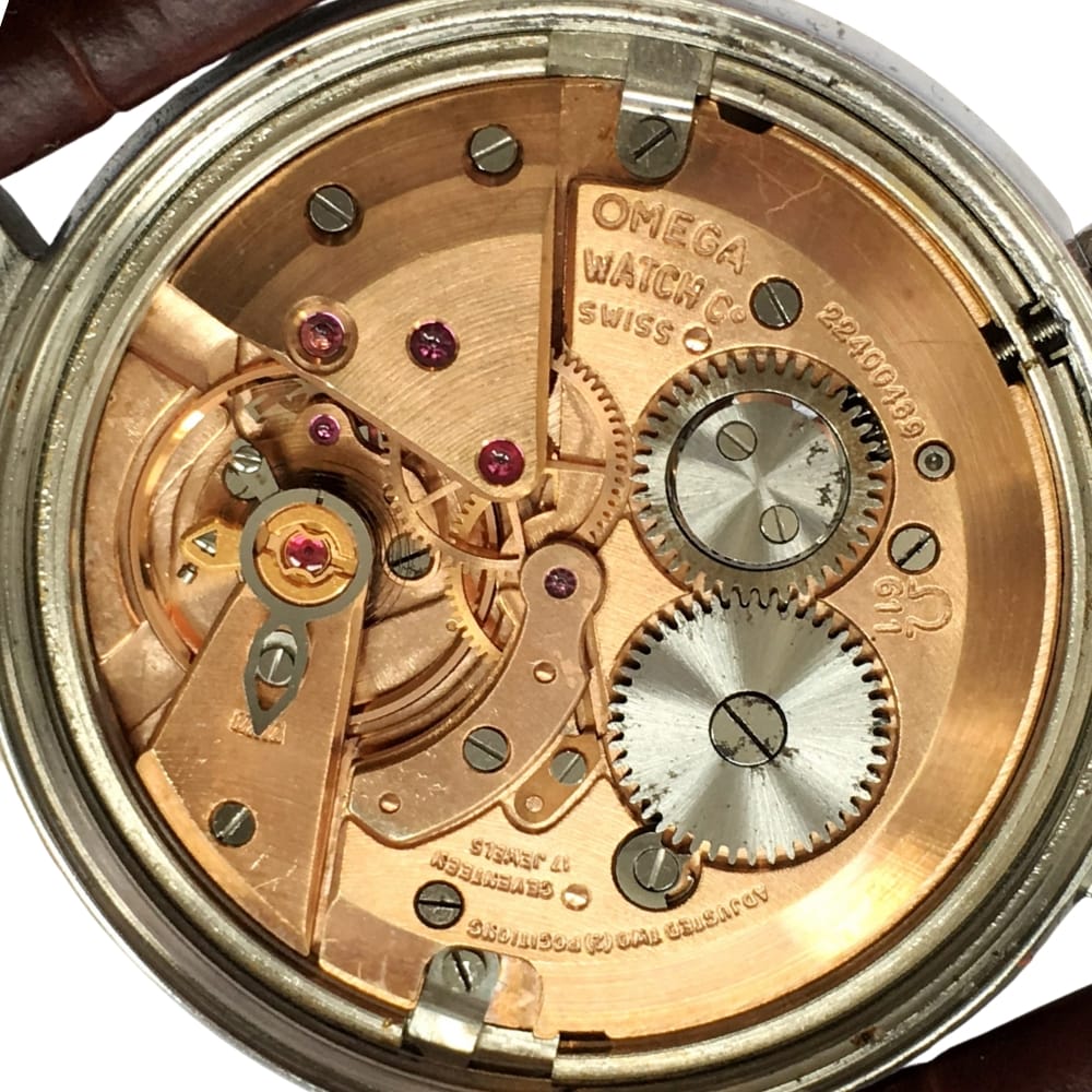 Close-up of an Omega Swiss watch movement showing gears, ruby jewels, and engraved text on copper parts.