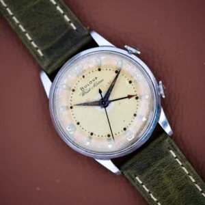 A Bulova Wrist Alarm Manual Wind Cal. 11AERC with a stainless steel case and green strap, displayed on a brown leather surface.