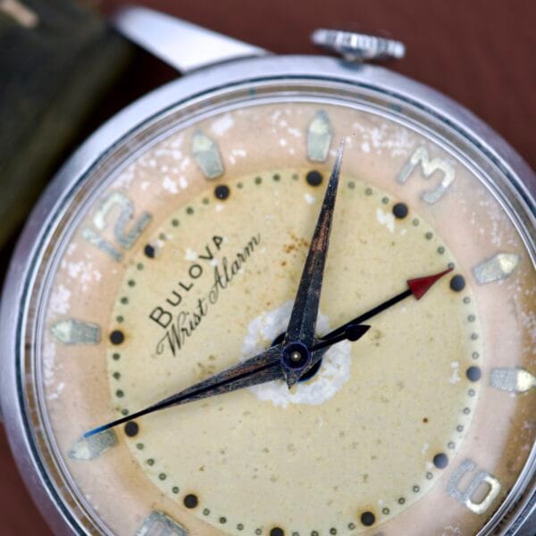 Close-up of a vintage Bulova Wrist Alarm Manual Wind Cal. 11AERC, featuring worn hands and a weathered dial in a classic stainless steel case.