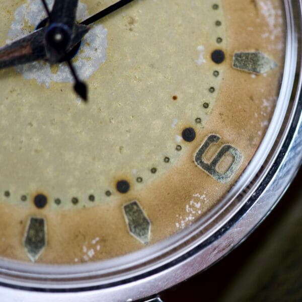 Close-up of a Bulova Wrist Alarm Manual Wind Cal. 11AERC featuring a weathered dial, black hour and minute hands, prominent number six, all set in a classic stainless steel case.