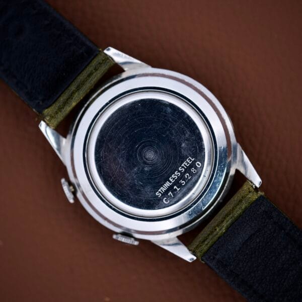 Close-up of the back of a Bulova Wrist Alarm Manual Wind Cal. 11AERC, showing "STAINLESS STEEL C 71380" engraved on its stainless steel case, against a brown background.