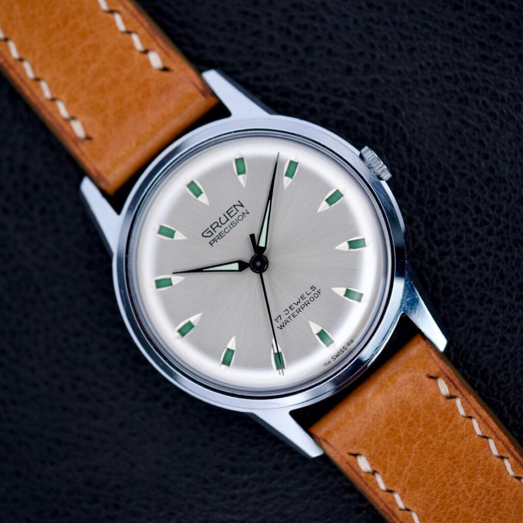 Gruen Precision 510 Caliber Day/Night Jump Hour Markers wristwatch with a tan leather strap, displayed on a black textured background.