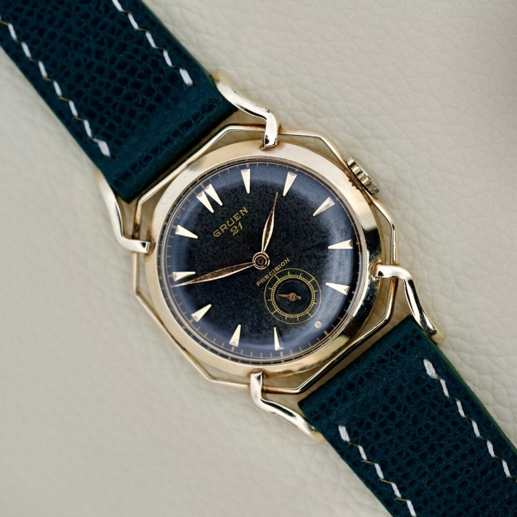 Gruen Barclay "Spider" Ref. 335-723 wristwatch featuring a black dial, gold case, 21 Jewels Cal. 335 movement, and a dark green stitched leather strap.