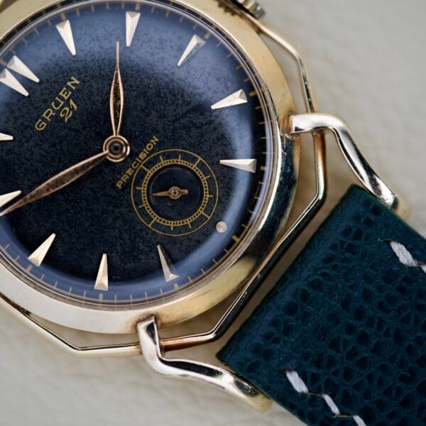 Close-up of a vintage Gruen Barclay "Spider" Ref. 335-723 wristwatch, showcasing a dark blue face, 21 Jewels Cal. 335 movement, and a textured dark strap.