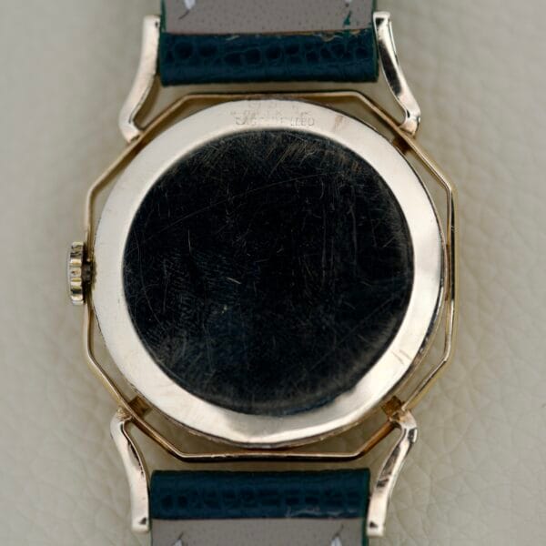 The back of a scratched Gruen Barclay "Spider" Ref. 335-723 21 Jewels Cal. 335 wristwatch with a dark green leather strap is displayed on a light surface.