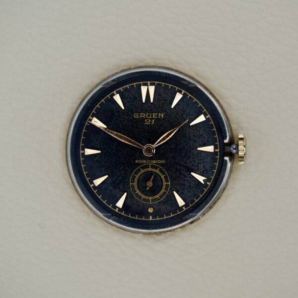A vintage black Gruen Barclay "Spider" Ref. 335-723 wristwatch face with gold hands and markers, featuring 21 Jewels Cal. 335, set against a light textured background.