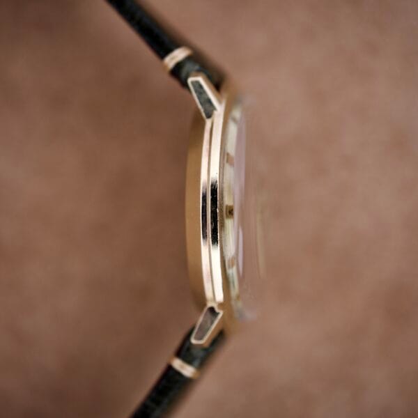 Side view of the slim gold Hamilton Masterpiece Electronic Date Ref. 981569 with Cal. 702 movement and black leather strap, set against a soft brown background.