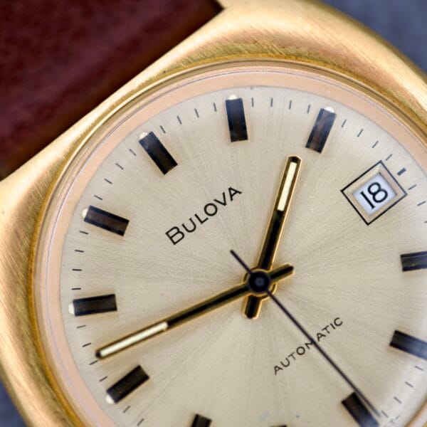 Close-up of a gold Bulova Cushion Case Automatic Ref. 7313-2 Cal. 11AOACD wristwatch, displaying the time 2:58 and date 18.