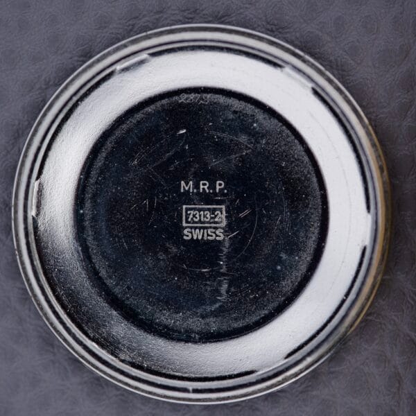 Round metal Bulova Cushion Case Automatic Ref. 7313-2 Cal. 11AOACD watch back, engraved "M.R.P. 7313-2 SWISS" in the center, displayed on a textured gray background.