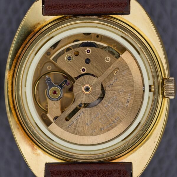 Close-up of the Bulova Cushion Case Automatic Ref. 7313-2 Cal. 11AOACD, featuring its exposed mechanical movement in a gold case with a brown leather strap.