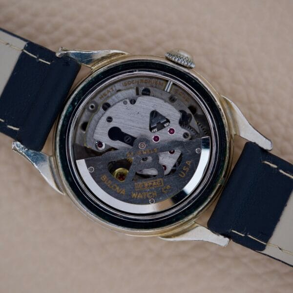 Close-up of the back of a Bulova 23 Jewels Automatic Six Adjustments Cal. 10BPAC wristwatch, revealing its exposed mechanical movement and intricate gears.