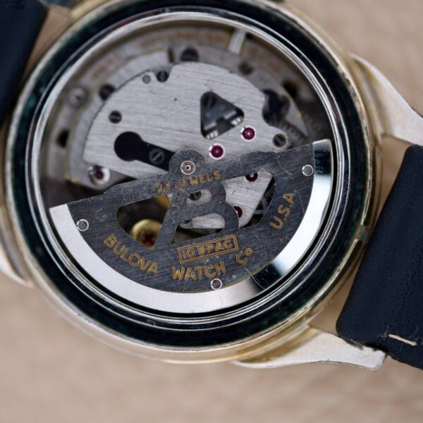 Close-up of a Bulova 23 Jewels Automatic Six Adjustments Cal. 10BPAC watch movement, showing visible gears and labeled Bulova Watch Co. USA.