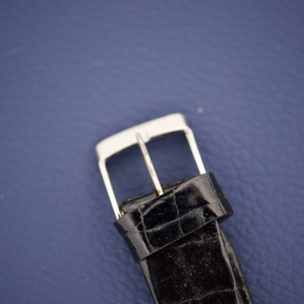 Close-up of a black leather strap with silver buckle on blue textured background, highlighting the elegance of the Piguette Antioch 17 Jewels Manual Wind Stainless Steel Case timepiece.