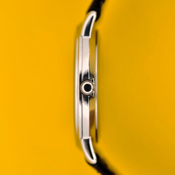 Side view of the Seiko Twin Quartz Ref. 9920-7000T Thin Stainless Steel wristwatch, showcasing its slim stainless steel case and black strap set against a vivid yellow background.