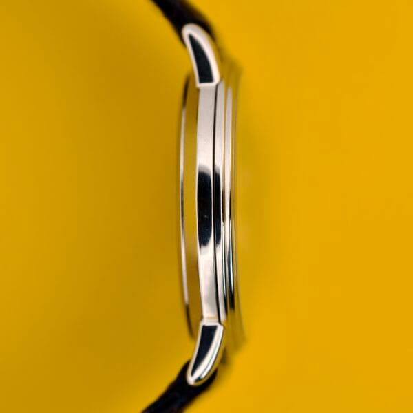 Close-up side view of a Seiko Twin Quartz Ref. 9920-7000T Thin Stainless Steel wristwatch with a black strap, set against a bright yellow background.