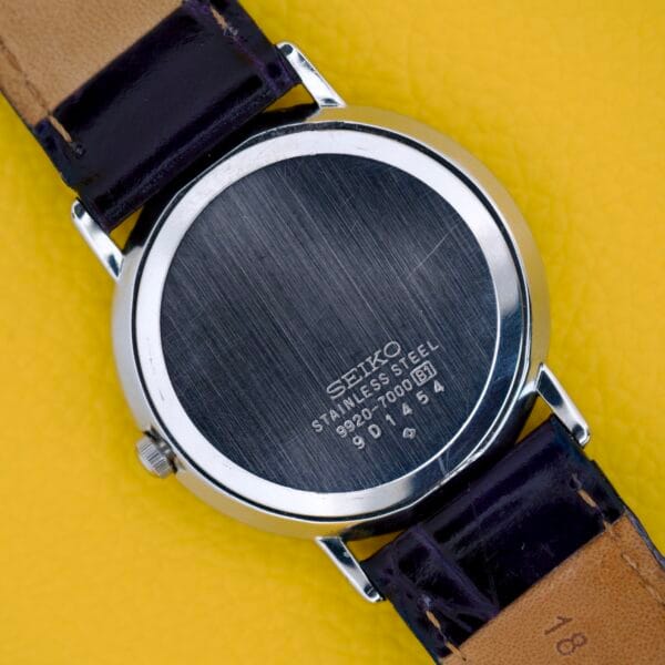 Back of a Seiko Twin Quartz Ref. 9920-7000T Thin Stainless Steel wristwatch showing model details and slim case, placed on a yellow textured surface.