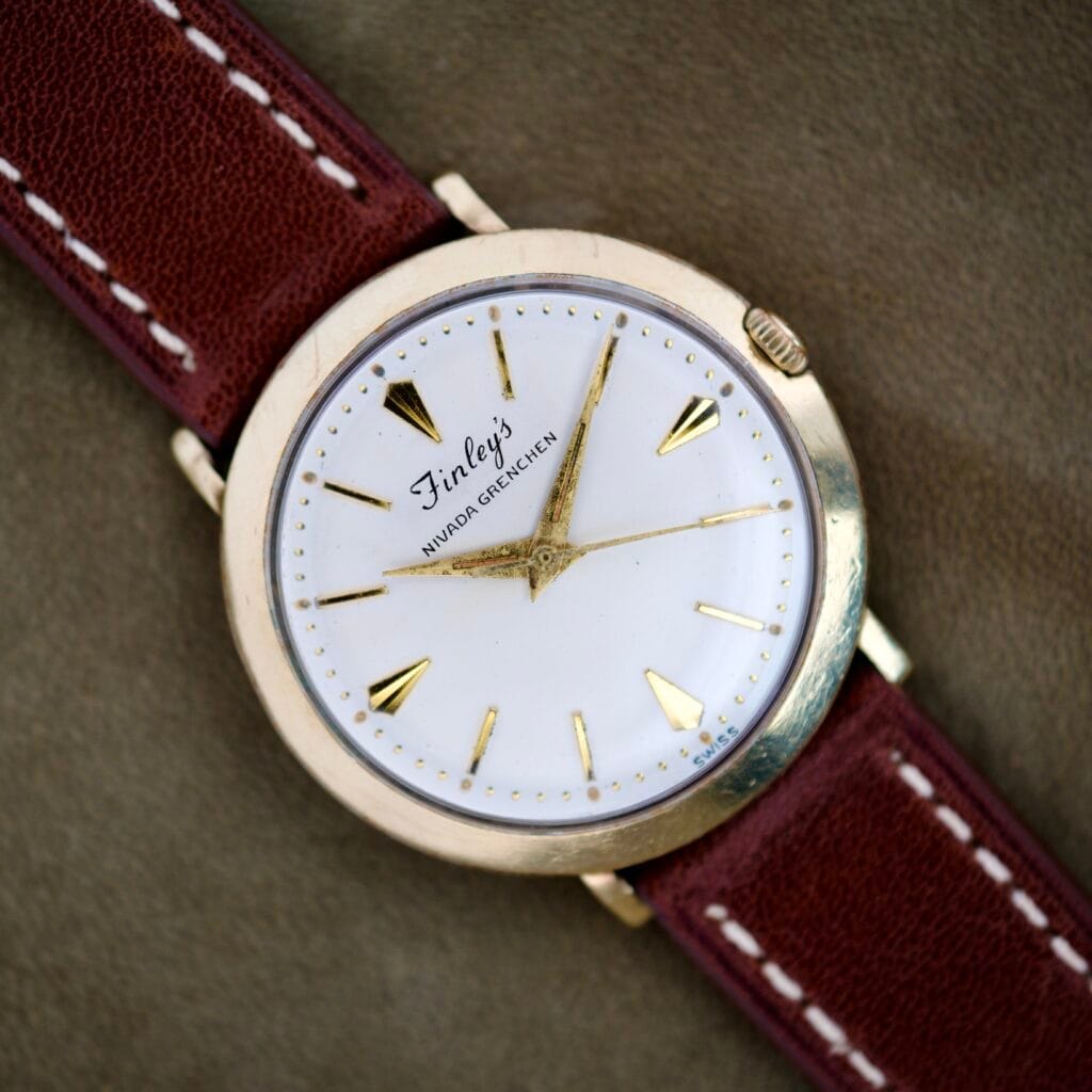 Finley's Nivada Grenchen Automatic with a white dial, gold hour markers and hands, and a brown leather band in a classic vintage design.