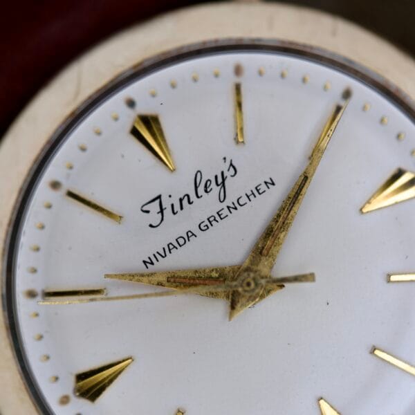 Close-up of Finley's Nivada Grenchen Automatic White Dial, featuring gold hands and hour markers on a striking white dial.