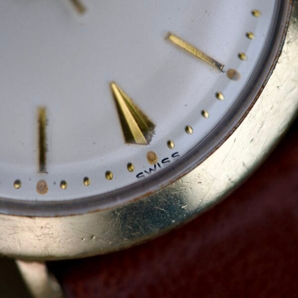 Close-up of Finley's Nivada Grenchen Automatic White Dial watch, featuring gold hour markers and "SWISS" near the edge.