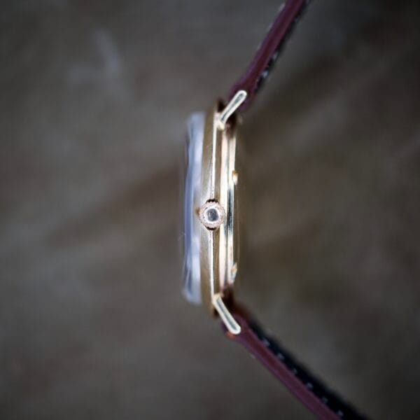 Side view of the Finley's Nivada Grenchen Automatic White Dial watch, featuring a gold case, brown leather strap, and white dial, with focus on the crown.