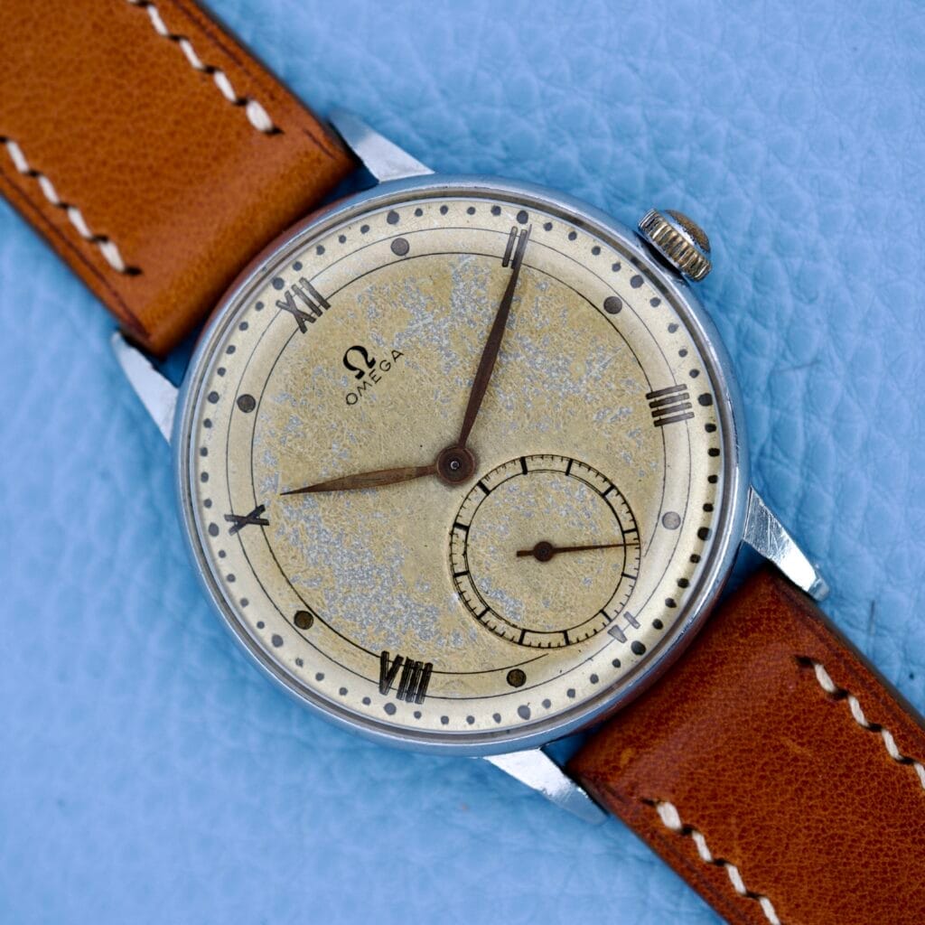 Omega Ref. 2319/2 Jumbo Case Manual Wind Cal. 30T2 wristwatch with a tan leather strap, displayed on a light blue textured surface.