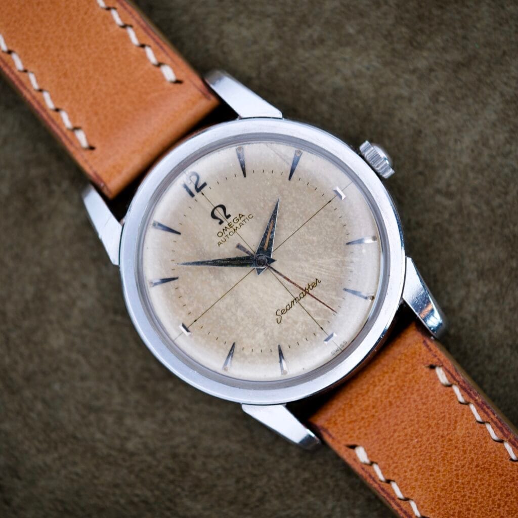 An Omega Seamaster Automatic Ref. 2846-1 with a Cross Hair Dial and tan leather strap is displayed on a textured brown surface.
