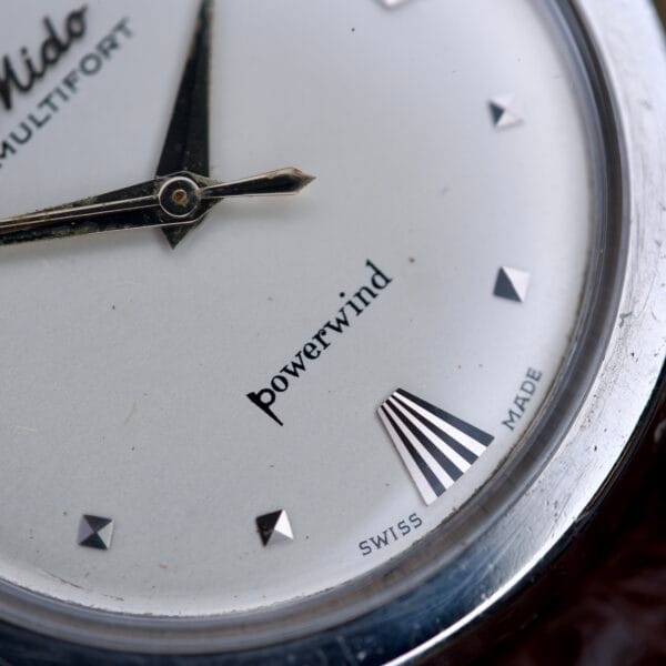 Close-up of the Mido Multifort Powerwind White Dial Automatic Cal. 917P watch face, featuring "Powerwind" text, hands, and "Swiss Made" at the bottom.